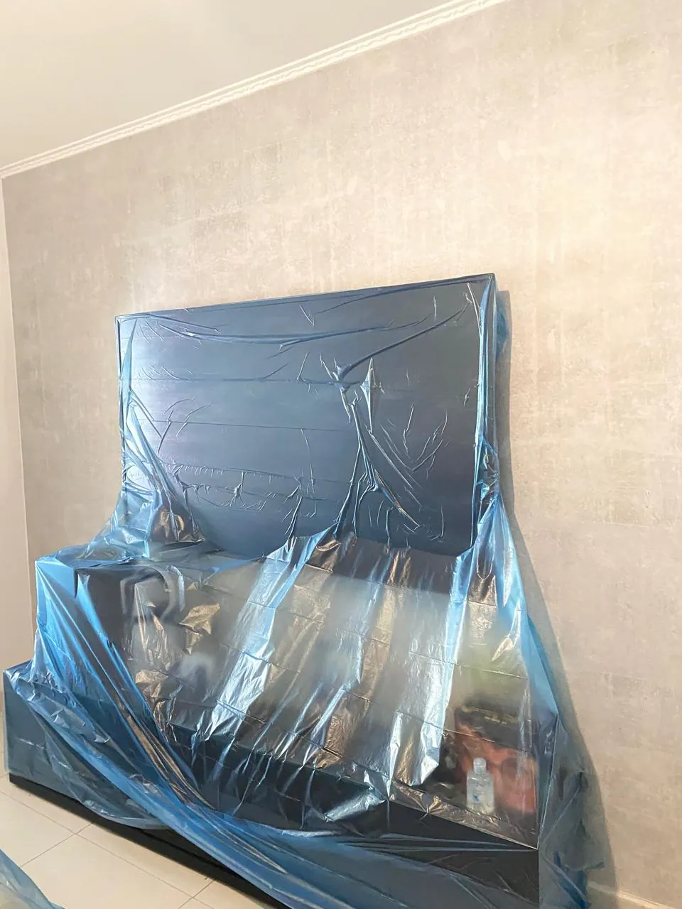 Cabeceira e cama protegidas com plástico durante a pintura do quarto